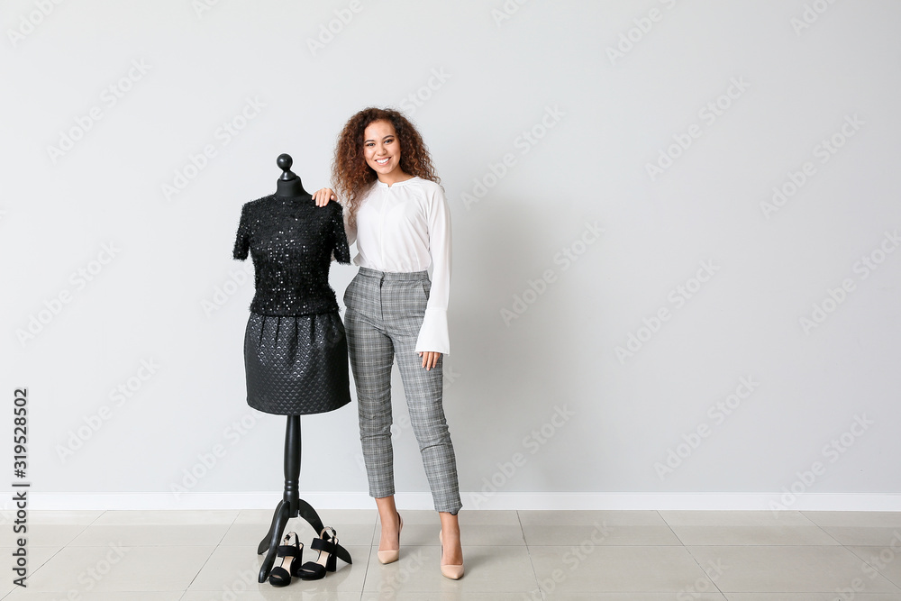 African-American stylist near mannequin against light wall