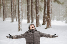 Portrait Of Boy Catching Snowflakes In Winter Forest