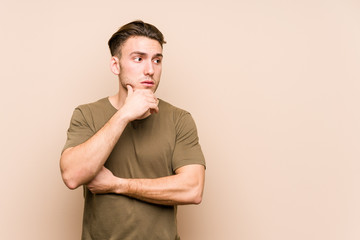 Wall Mural - Young caucasian man posing isolated thoughtful looking to a copy space covering mouth with hand.