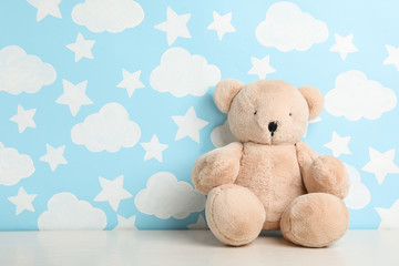 Wall Mural - Teddy bear on white table near wall with painted blue sky, space for text. Baby room interior