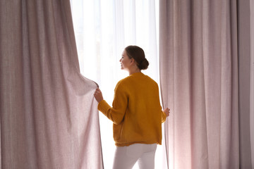 Wall Mural - Woman opening window curtains at home in morning