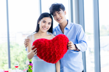 Valentine's day concept,asian Young happy sweet couple Abstract blur with focus show in love holding a red heart shaped pillow After lunch In a restaurant background