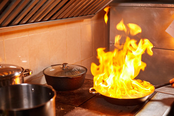 Flambe. Fire in frying pan. Professional chef in a commercial kitchen cooking. Man frying food in flaming pan on hob in outdoor kitchen