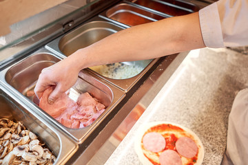 Wall Mural - Cooking pizza. Lays out the cheese and ham filling, ingredients on the dough preform. Closeup hand of chef baker in uniform white apron cook at kitchen