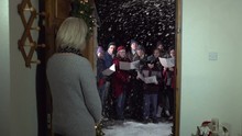 Carol Singers At Christmas Singing Outside - Women Opens Front Door -Snowing - View From Inside, Crane Shot - Stock Video Clip Footage
