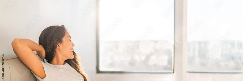 Clean indoor air happy Asian woman breathing at home from air purifier sitting in sofa looking out the window panoramic banner. - obrazy, fototapety, plakaty 