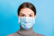 Portrait Of Young Woman Wearing Medical Mask At Blue Background. Protect Your Health. Coronavirus Concept
