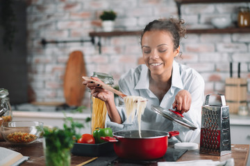 Young woman in kitchen. Beautiful mixed race woman cooking pasta. 