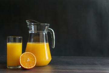 Orange juice in decanter and glass with half of orange on dark wooden brown background. Copy space. Horizontal orientation. 