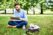 © baranq - Handsome young man sitting on grass in park with tablet during lunch break