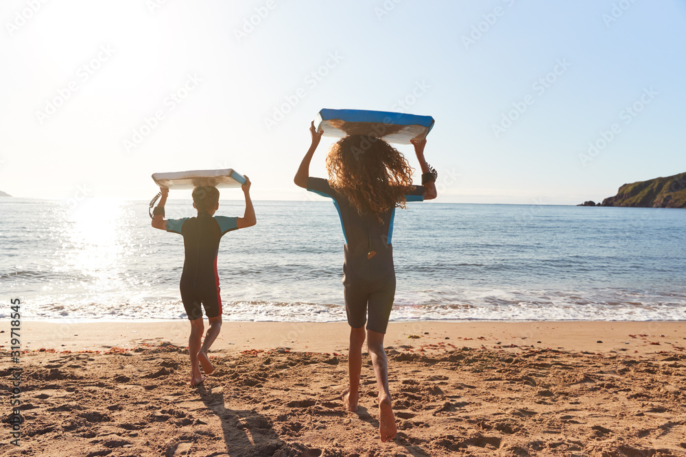 Rear View Of Children In Wetsuits Carrying Bodyboards On Summer Beach ...