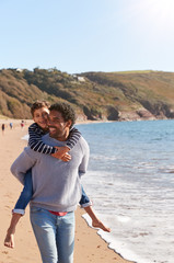 Loving Father Giving Son Piggyback As They Walk Along Winter Beach Together