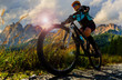 canvas print picture - Tourist cycling in Cortina d'Ampezzo, stunning rocky mountains on the background. Woman riding MTB enduro flow trail. South Tyrol province of Italy, Dolomites.