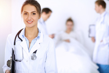 Female doctor smiling on the background with patient in the bed and two doctors