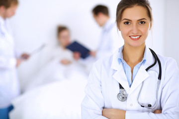 Wall Mural - Female doctor smiling on the background with patient in the bed and two doctors