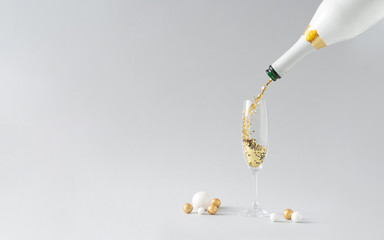 champagne bottle pouring golden glitter into the glass with white and golden decoration against grey