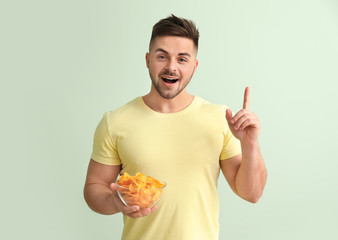 Handsome young man with tasty potato chips and raised index finger on color background