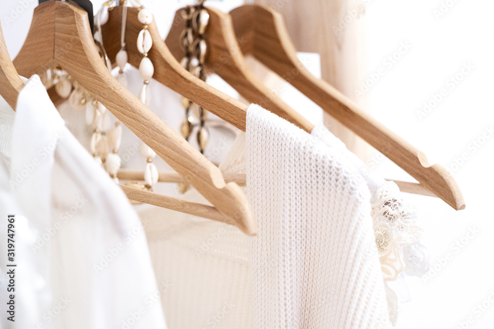 Detail of white clothes hanging on wooden hangers in a fashion store. - obrazy, fototapety, plakaty 