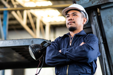 Asian Mechanic engineering in safety Mechanic suit and hard hat standing arms crossed at truck and Forklift Maintenance garage.