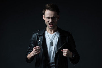 angry stylish brutal man in biker jacket showing fists isolated on black