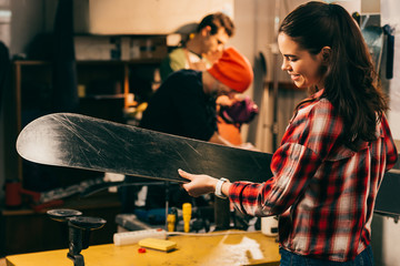 Wall Mural - smiling worker holding ski and colleagues on background in repair shop