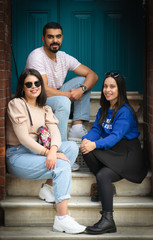 three friends are sitting on the stairs in Balat, Turkey.Male person surounded by two attractive young girls in casual clothes and the background of gren door. Multicultural environment. Balat. Turkey