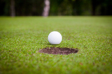 Wall Mural - Golf ball on green meadow. golf ball on lip of cup