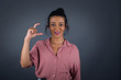© Jihan - Blonde European woman over isolated background gesturing with hand showing small size, measure symbol. Smiling looking at the camera. Measuring concept.