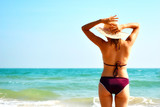 Fototapeta  - Woman in hat on the beach. Girl in a swimsuit in the ocean. Tropical summer vacation