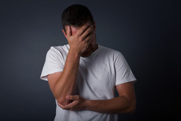 Indoor portrait of handsome man with stylish haircut, wearing casual clothes, making facepalm gesture while smiling, standing over gray background amazed with stupid situation.