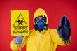 A man in a protective chemical mask and a protective yellow suit with a banner in his hand with the words biohazard shows a stop sign. Biohazard concept