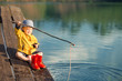 Little boy siting on wooden dock and fishing at sunset.