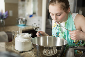 young girl licking batter from mixer paddles