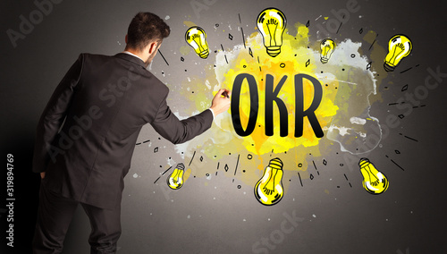 businessman drawing colorful light bulb with OKR abbreviation, new technology idea concept