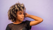 © Camilorico_graphy - Mujer joven afrodecendiente cabello risado suelto con su braso levantado mostrando levemente su mano, mirando hacia un lado sobre fondo morado