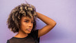 © Camilorico_graphy - Mujer joven afrodecendiente cabello risado suelto con su braso levantado ocultando su mano entre su cabello, mirando hacia un lado sobre fondo morado
