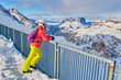 Woman skier taking a break and enjoying the mountain views towards Sassolungo and Sella group in Dolomites, Italy, from a viewpoint at Serauta cable car stop on Marmolada glacier.