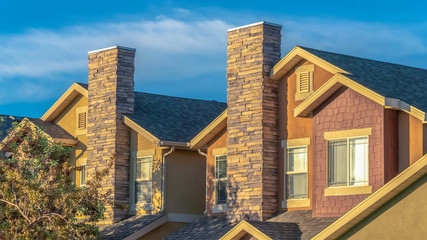 Wall Mural - Panorama Sunny day view of home facade with stone brick chimneys and gable roofs