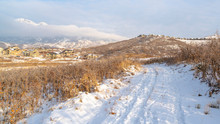 Panorama Frame Road On Hill With Snow Overlooking Houses And Mountain Against Cloudy Sky
