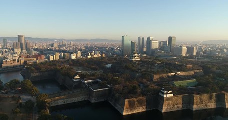 Wall Mural - Historic Osaka castle in the city surrounded by stone walls and moat – aerial flying at sunrise.