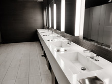 Public Empty Restroom With Washstands, Baby Changer, And Toillets In Mirror. White Sink Row With Mirrors And Lights. Top Horizontal View Copyspace