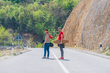 Wall Mural - Two male longboarders carrying their longboards in their hands while climbing uphill and preparing for a downhill slide. Wearing red t-shirts, green hat, and super cool sunglasses.