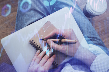 Double exposure of man doing notes of stock market with forex graph.