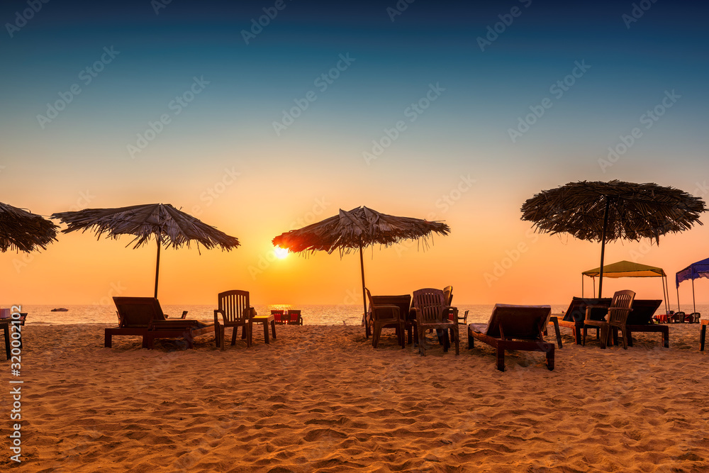 Sun umbrellas with lounge chairs at sunset on a tropical sunny beach in GOA, India - obrazy, fototapety, plakaty 