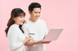 © makistock - Great credit offer. Cheerful asian couple shopping online on laptop with bank card on pink studio background