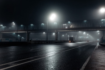 Foggy misty night road and overhead pedestrian bridge illuminated by street lights