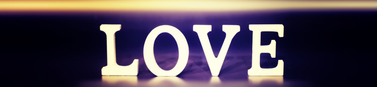 Wooden and metal letters forming word LOVE written on dark black background with lights.