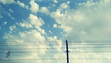 LOW ANGLE VIEW OF Barbed Wire Fence AGAINST CLOUDY SKY