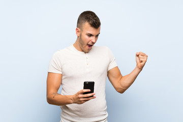 Wall Mural - Young handsome blonde man over isolated blue background using mobile phone