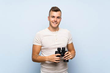 Wall Mural - Young handsome blonde man over isolated blue background with black binoculars